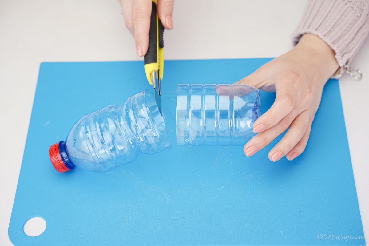 A craft knife cutting an empty plastic bottle in half.