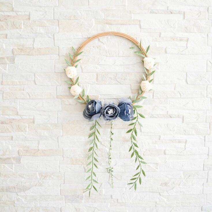 Denim Blooms Door Wreath 6 A woman proudly holding her handmade denim floral wreath in front of a rustic door, showcasing its beauty.